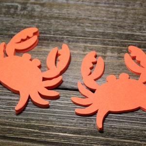 May include: Two orange foam cutout crabs on a wood background.