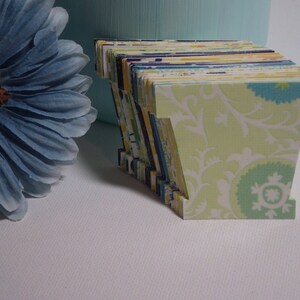 May include: A stack of light green paper letters with a white floral pattern. The letters are stacked to form the letter "V".