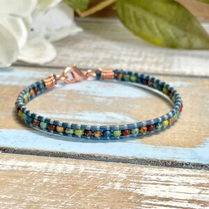 May include: A blue leather bracelet with a copper clasp and colorful beads. The bracelet is on a wooden surface.