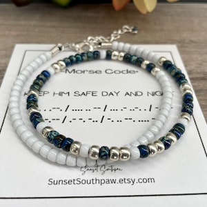 May include: Two beaded bracelets, one white and one blue with silver beads, with a card that reads "Morse Code" and "Keep him safe day and night" with the Morse code translation below.