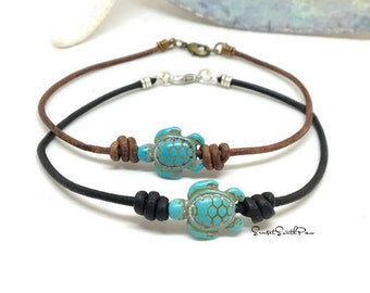 May include: Two leather bracelets with turquoise turtle charms. The top bracelet is brown leather with a silver clasp. The bottom bracelet is black leather with a black knot. Both bracelets feature the text "Sunset South Paw".