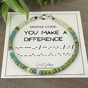 May include: A beaded bracelet featuring turquoise, lime green, and cream-colored beads with a silver-toned lobster clasp. The bracelet is displayed on a white card printed with the text MORSE CODE YOU MAKE A DIFFERENCE and Morse code symbols.