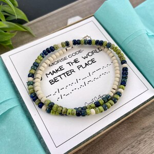 May include: A beaded bracelet with green, blue, and white beads. The bracelet is displayed on a card with the text "Morse Code - Make the World a Better Place" and the message in Morse code.