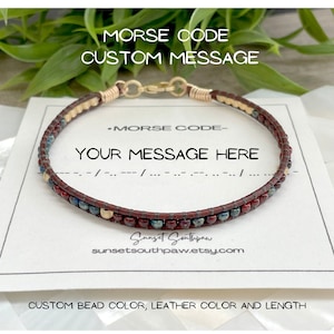 May include: A brown leather bracelet with red, blue, and gold beads. The bracelet is on a white card with the text "MORSE CODE CUSTOM MESSAGE" and "YOUR MESSAGE HERE".