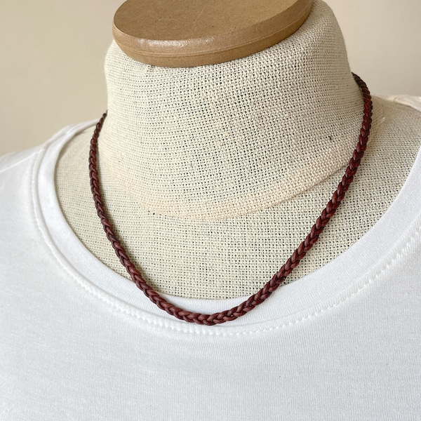 May include: A braided brown leather necklace displayed on a mannequin. The necklace is a simple, elegant design, perfect for everyday wear. The necklace is approximately 18 inches in length.
