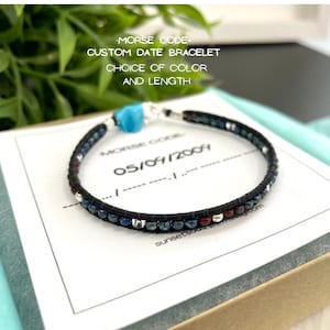 May include: A black leather bracelet with blue, red, and silver beads. The bracelet is in a box with a white card that says "MORSE CODE- CUSTOM DATE BRACELET CHOICE OF COLOR AND LENGTH" and "05/09/2004".