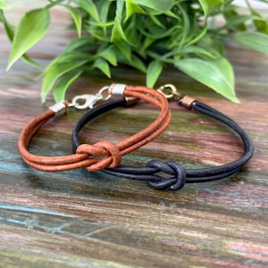 May include: Two leather bracelets with knotted closures. One bracelet is brown and the other is black.