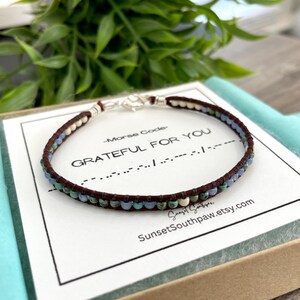 May include: A brown leather bracelet with turquoise, blue, and white beads. The bracelet is on a white card with the text "Morse Code - GRATEFUL FOR YOU" and a series of dots and dashes. The card also includes the text "SunsetSouthpaw.etsy.com".