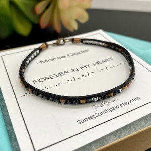 Peut inclure: Un bracelet noir à perles avec des perles argentées et dorées. Le bracelet est dans une boîte avec une carte blanche qui dit "Morse Code - FOREVER IN MY HEART" et le code Morse pour la phrase. La carte a également l'adresse du site Web SunsetSouthpaw.etsy.com.