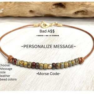 May include: A brown leather bracelet with a gold clasp and a row of colorful beads. The beads are a mix of yellow, red, and gold. The bracelet has the text "Bad A$$" and "~PERSONALIZE MESSAGE~" on it. Choose from a variety of options, including message, size, leather, bead colors, and Morse code.