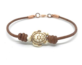 May include: A brown leather bracelet with a white turtle charm. The bracelet has a copper clasp.