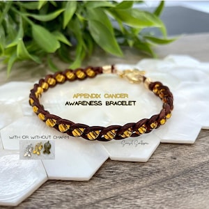 May include: Brown braided bracelet with gold beads. The bracelet is labelled "Appendix Cancer Awareness Bracelet" and "With or Without Charm".