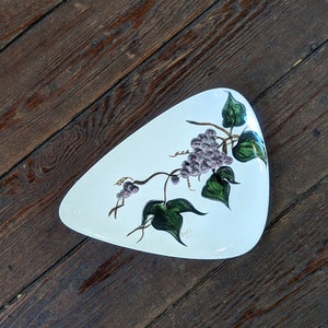 May include: White ceramic serving dish with a grapevine design. The dish is shaped like a leaf and has a green and purple grapevine design with green leaves.