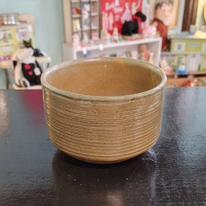 May include: A brown ceramic bowl with a light green glaze and a ribbed texture. The bowl is empty and sitting on a dark surface.