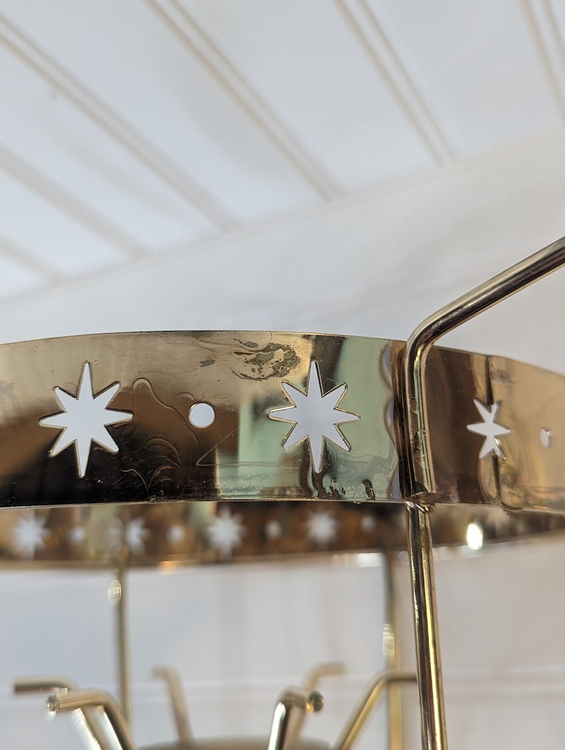 May include: Gold metal stand with a round top and three legs. The top of the stand has a decorative design of white stars.