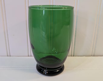 May include: A green glass tumbler with a black base. The glass is a vibrant green color and has a smooth, rounded shape. The base is a solid black color. The tumbler is likely used for drinking beverages.
