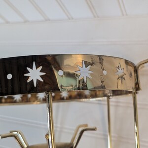 May include: Gold metal candle holder with a round top and star cutouts. The holder has three arms that extend from the base.
