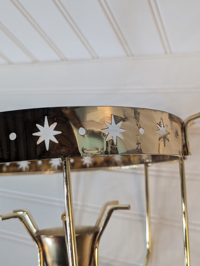 May include: Gold metal candle holder with a round top and star cutouts. The holder has three arms that extend from the base.