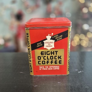 May include: A rectangular red and gold metal Eight O'Clock Coffee tin with a lid. The front features a black diagonal banner with the text Bean Coffee, Ground to Order, and A Rich, Mellow Blend. Below is the text Eight O'Clock Coffee.
