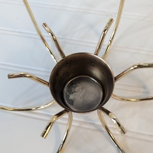 May include: Gold metal candle holder with a circular base and six arms that curve upwards. The holder is designed to hold six candles.