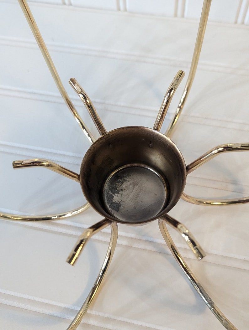May include: Gold metal candle holder with a circular base and six arms that curve upwards. The holder is designed to hold six candles.