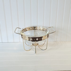 May include: A clear glass serving dish with a gold rim and white star accents sits on a gold metal stand with three legs.