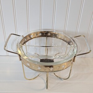 May include: A gold-toned metal serving stand with a clear glass bowl. The bowl has a gold rim and a star pattern. The stand has three legs.