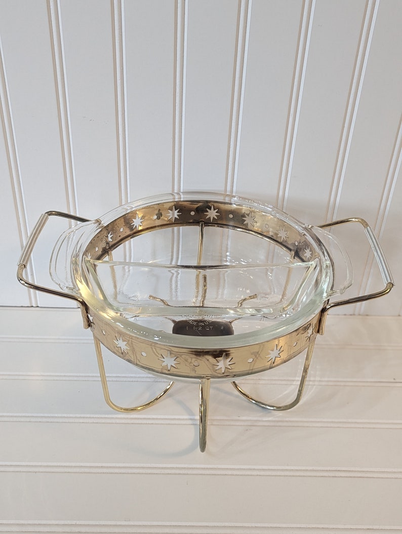 May include: A gold-toned metal serving stand with a clear glass bowl. The bowl has a gold rim and a star pattern. The stand has three legs.