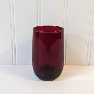 May include: A deep red glass tumbler with a rounded bottom. The glass is clear and has a smooth surface.