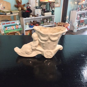 May include: White ceramic planter shaped like a person riding in a wagon. The planter has a distressed look and is perfect for small plants or succulents.