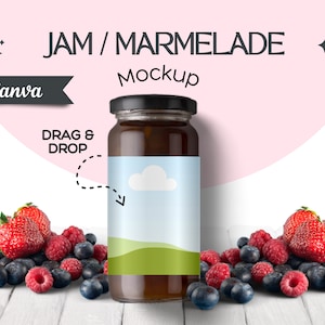 May include: A glass jar of jam or marmalade with a blue and green label featuring a white cloud and green hills. The jar is sitting on a white wooden surface with a pile of fresh berries in front of it. The text on the label says "DRAG & DROP".
