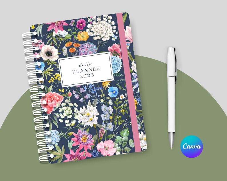 May include: A daily planner with a floral design. The cover features a variety of flowers in shades of pink, blue, white, and yellow on a dark blue background. The planner has a pink and white striped spine and a silver coil binding. The text "daily planner 2023" is printed in white on a white rectangle.