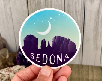 Peut inclure: Un autocollant rond avec un fond dégradé bleu, vert et violet. L'autocollant présente une silhouette de chaîne de montagnes avec une lune croissante et des étoiles dans le ciel. Le texte "SEDONA" est imprimé en blanc au bas de l'autocollant.