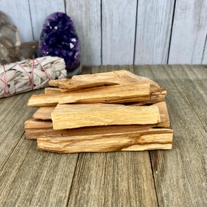 May include: A stack of Palo Santo sticks, a type of fragrant wood used for smudging and spiritual cleansing. The sticks are light brown and have a natural, rough texture.