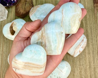 Peut inclure: Plusieurs pierres polies en forme de cœur en calcite rubanée bleu clair et blanc. Les pierres présentent des surfaces lisses et brillantes avec des couches minérales naturelles visibles dans des tons bleu pâle, crème et beige.