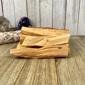 May include: A stack of Palo Santo sticks, a type of fragrant wood used for smudging and spiritual cleansing. The sticks are light brown and have a natural, rough texture.