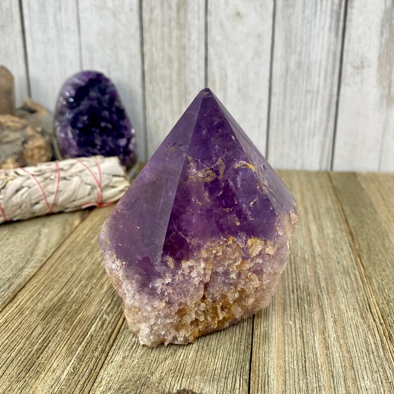 K&ouml;nnte beinhalten: Eine gro&szlig;e, violette Amethyst-Kristallspitze mit einer nat&uuml;rlichen, rauen Basis. Der Kristall ist klar und hat einen leichten goldenen Farbton.