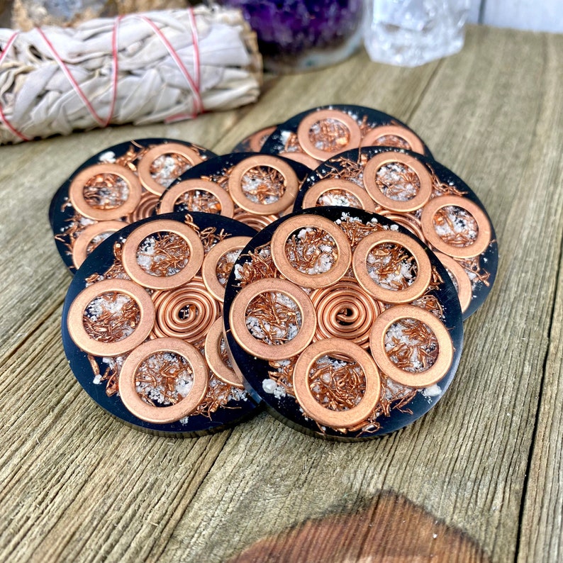 Peut inclure: Un ensemble de six sous-verres en r&eacute;sine noire avec du fil de cuivre et des anneaux de cuivre incrust&eacute;s dans la r&eacute;sine. Les sous-verres ont un aspect mouchet&eacute; blanc.