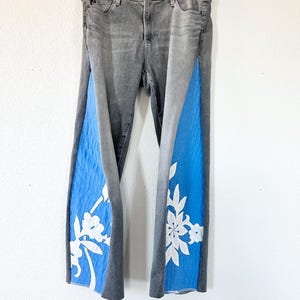 May include: Gray denim jeans with blue panels on the legs. The panels have white floral embroidery.