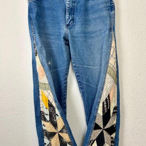 Op de afbeelding: Blauwe spijkerbroek met patchwork quilt accenten langs de buitenste naden. Het patchwork heeft een verscheidenheid aan stoffen in tinten zwart, cr&egrave;me, geel en roze. De jeans hebben een klassiek ontwerp met vijf zakken.