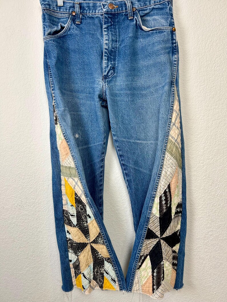 Op de afbeelding: Blauwe spijkerbroek met patchwork quilt accenten langs de buitenste naden. Het patchwork heeft een verscheidenheid aan stoffen in tinten zwart, cr&egrave;me, geel en roze. De jeans hebben een klassiek ontwerp met vijf zakken.