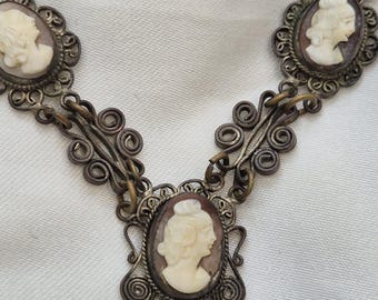 Peut inclure: Un collier en filigrane argenté avec trois pendentifs camée représentant des profils de femmes. Les camées sont sertis dans des cadres ovales et ont un fond brun.