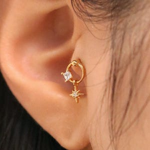 May include: Gold hoop earring with a small square-shaped clear gemstone and a dangling star charm with a smaller clear gemstone in the center.