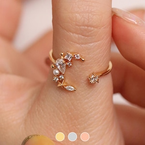 Peut inclure: Bague en or avec un motif de croissant de lune orné de petites pierres blanches et d'une perle. La bague est portée sur un doigt.