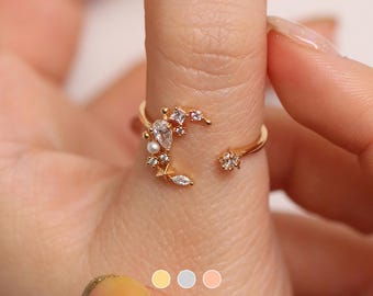 May include: Gold ring with a crescent moon design adorned with small white stones and a pearl. The ring is on a finger.