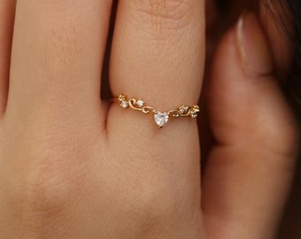 May include: A delicate gold ring with a small heart-shaped diamond in the center. The ring is adorned with smaller diamonds and intricate floral designs.
