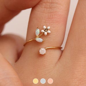 May include: A gold ring with a delicate flower design featuring white opal stones. The ring is adjustable and can be worn on any finger.