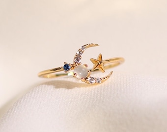 May include: A gold ring with a crescent moon design, a small star, and a white stone. The moon is accented with small clear stones.