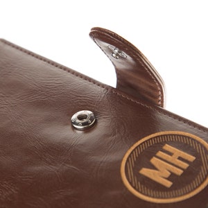 May include: A brown leather journal with a flap closure and a metal button. The journal has a personalised engraved wooden circle with the initials "MH" on the front.