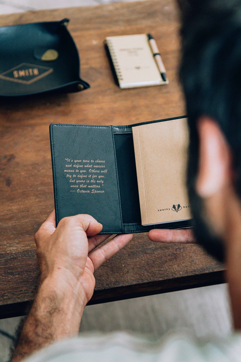 May include: A black leather notebook with a gold embossed quote by Octavia Spencer: "It's your turn to choose and define what success means to you. Others will try to define it for you, but yours is the only voice that matters."